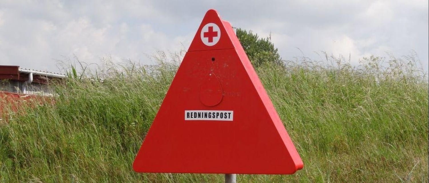 Rød trekantet redningspost ved græsareal